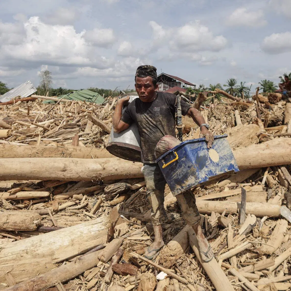 A man carries belongings he recovered from among piles of uprooted trees swept by the flash flood in Aceh Tamiang, Northern Sumatra, on Dec 11.
