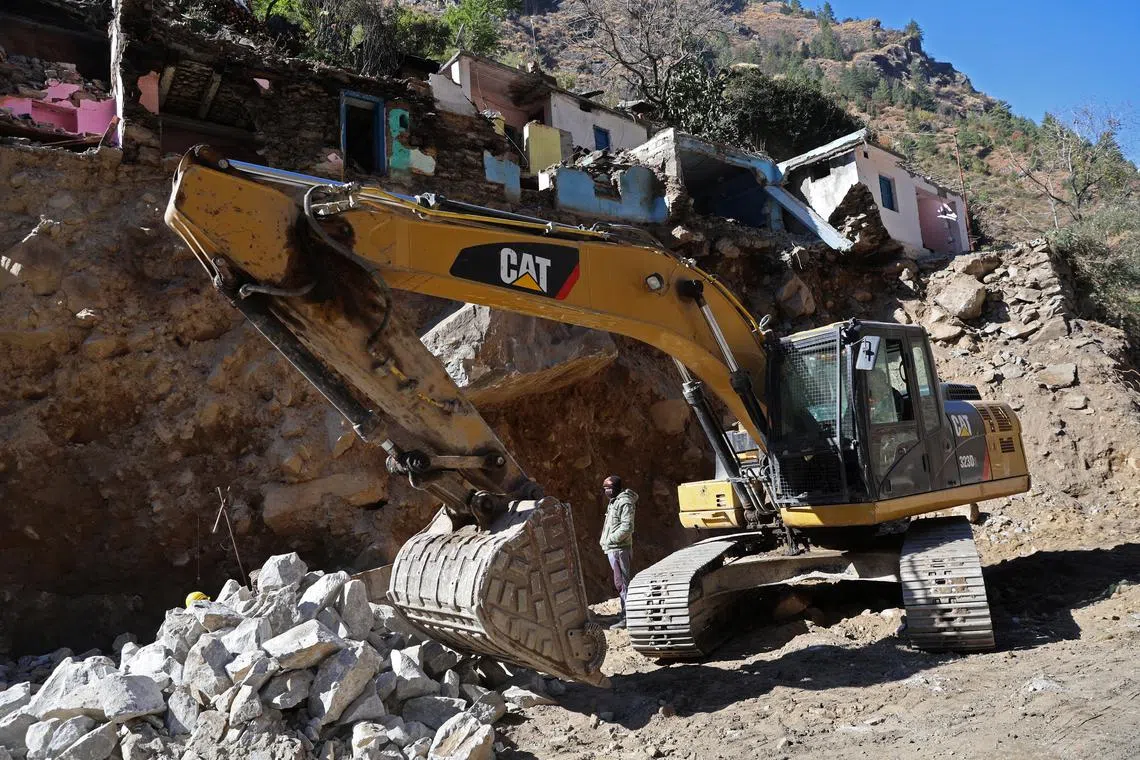 A worker stands next to an excavator as it removes stones flanking the national highway ahead of road widening, below houses once belonging to people who have since been moved out and received financial compensation, around 30km from Joshimath, in the northern state of Uttarakhand, India, Jan 15, 2023. 
