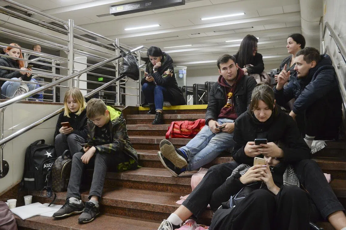 People check their phones as they shelter inside a metro station amid Russian shelling in Kyiv, on Oct 31, 2022.