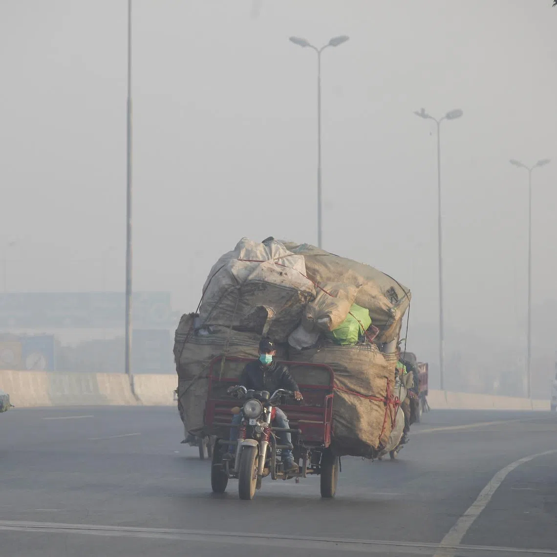 FILE PHOTO: A man rides a motor tricycle, loaded with sacks of recyclables, amid dense smog in Lahore, Pakistan November 24, 2021. REUTERS/Mohsin Raza/File Photo