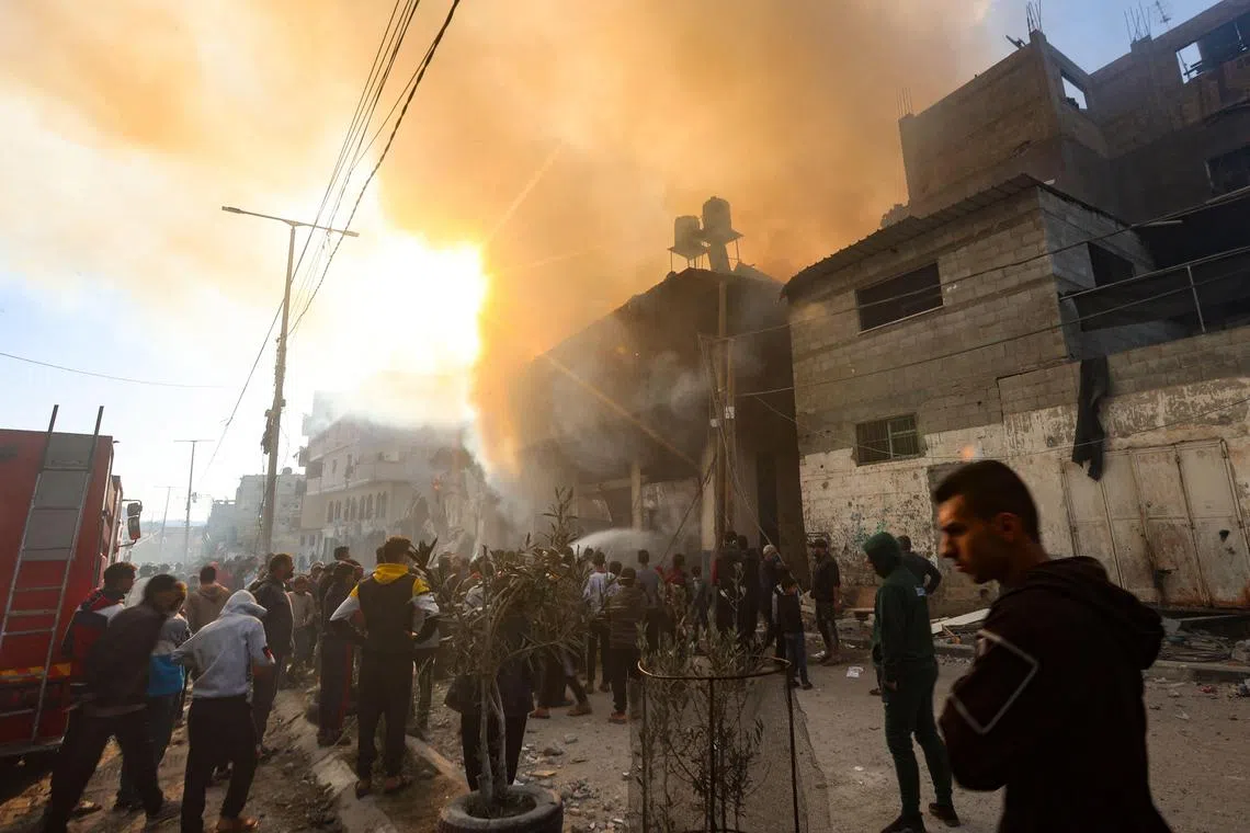 TOPSHOT - People gather in front of a burning building after it was hit by an Israeli strike in Khan Yunis in the southern Gaza Strip on December 9, 2023. Israel pressed its offensive against Hamas militants in Gaza on December 9, after the United States blocked an extraordinary UN bid to call for a ceasefire in the two-month war. (Photo by AFP)