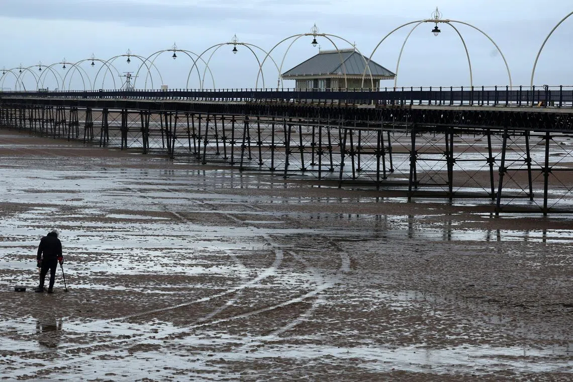 A man using a metal detector on the beach in front of Southport Pier, which has been closed for over a year for safety and structural reasons in Southport, Britain, Feb 20, 2024. 