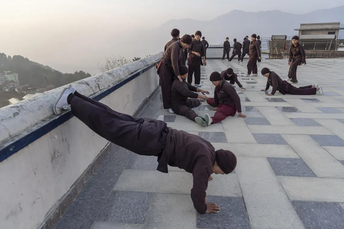 Nuns warm up before an early morning kung fu lesson at Druk Amitabha Nunnery, on a hill overlooking Kathmandu, Nepal, Feb. 4, 2023. In Himalayan Buddhism, the religious roles of nuns have long been restricted by rules and customs, but one sect is changing that, mixing meditation with martial arts and environmental activism. (Saumya Khandelwal/The New York Times)