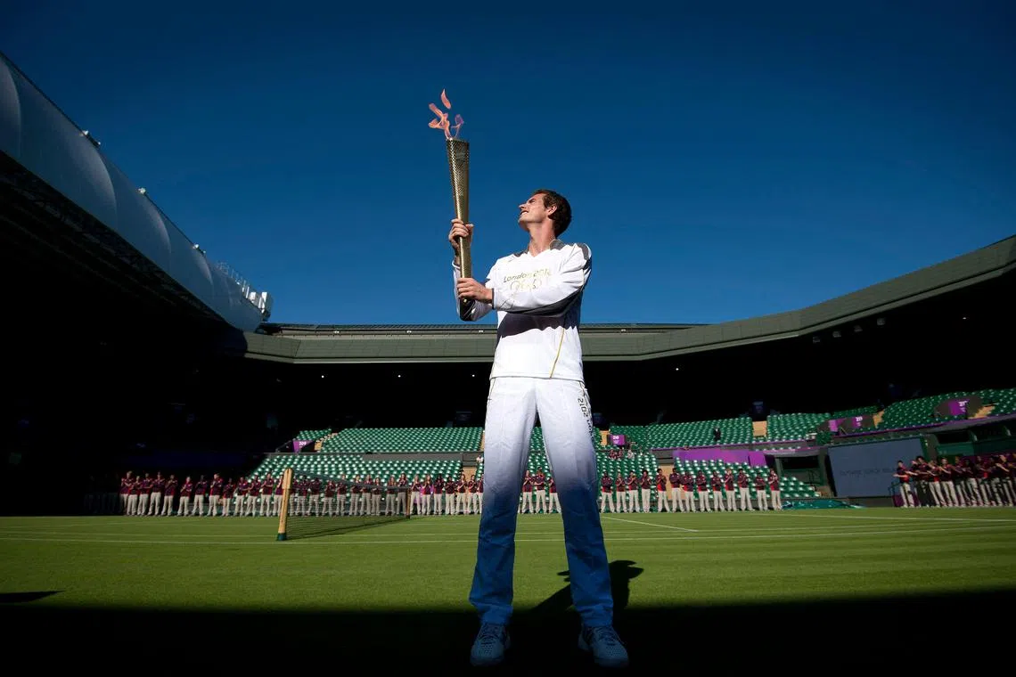 Andy Murray carries the Olympic torch on Centre Court at the All England Tennis Club in Wimbledon, before the start of the London 2012 Olympic Games. 