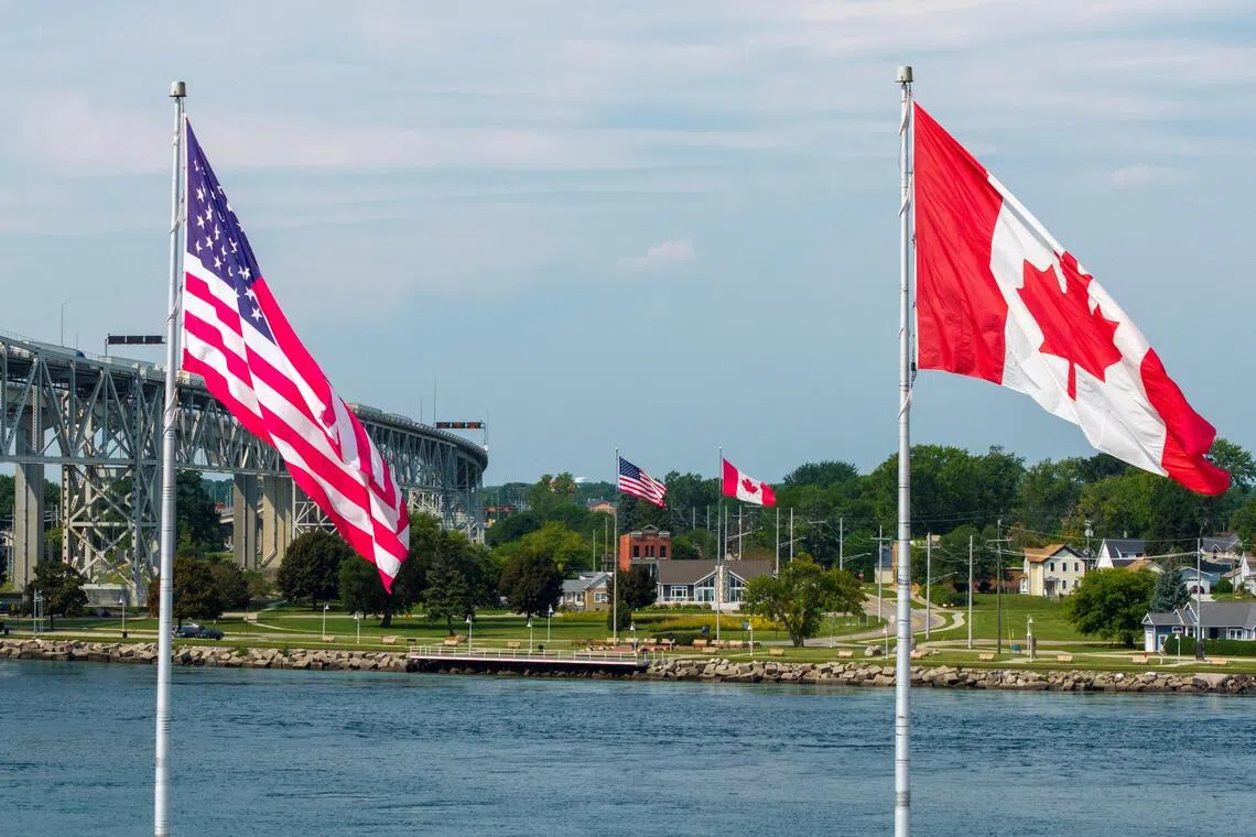 Canadian and US flags fly on both sides of the St Clair River near the Blue Water Bridge, connecting Sarnia, Ontario, and Port Huron, Michigan.