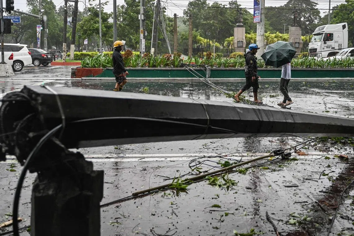 People walking past a fallen electrical post brought down by strong winds from weather due to Tropical Storm Yagi in Manila on Sept 2. 