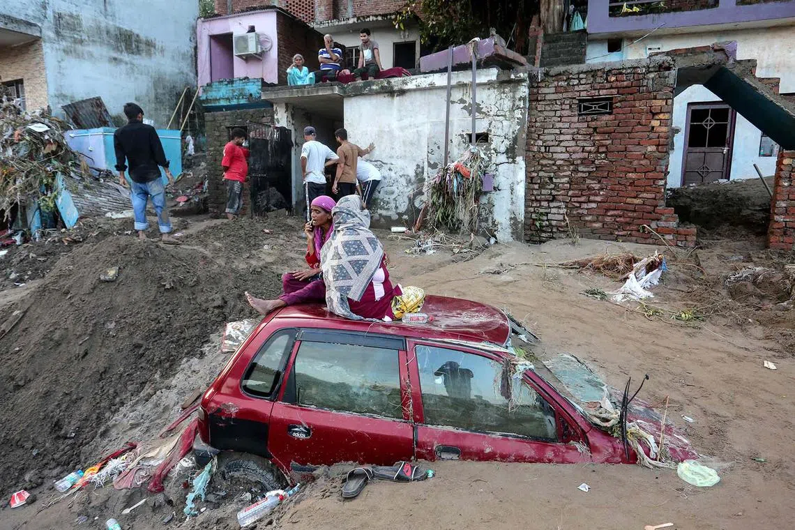 Women sitting on a car buried under mud and debris along the banks of the overflowing Tawi river after heavy rains induced flooding in Jammu on Aug 27, 2025. Floods and landslides triggered by record-breaking heavy rain have killed more than 30 people in India's Himalayan region of Jammu and Kashmir, officials said on Aug 27. 