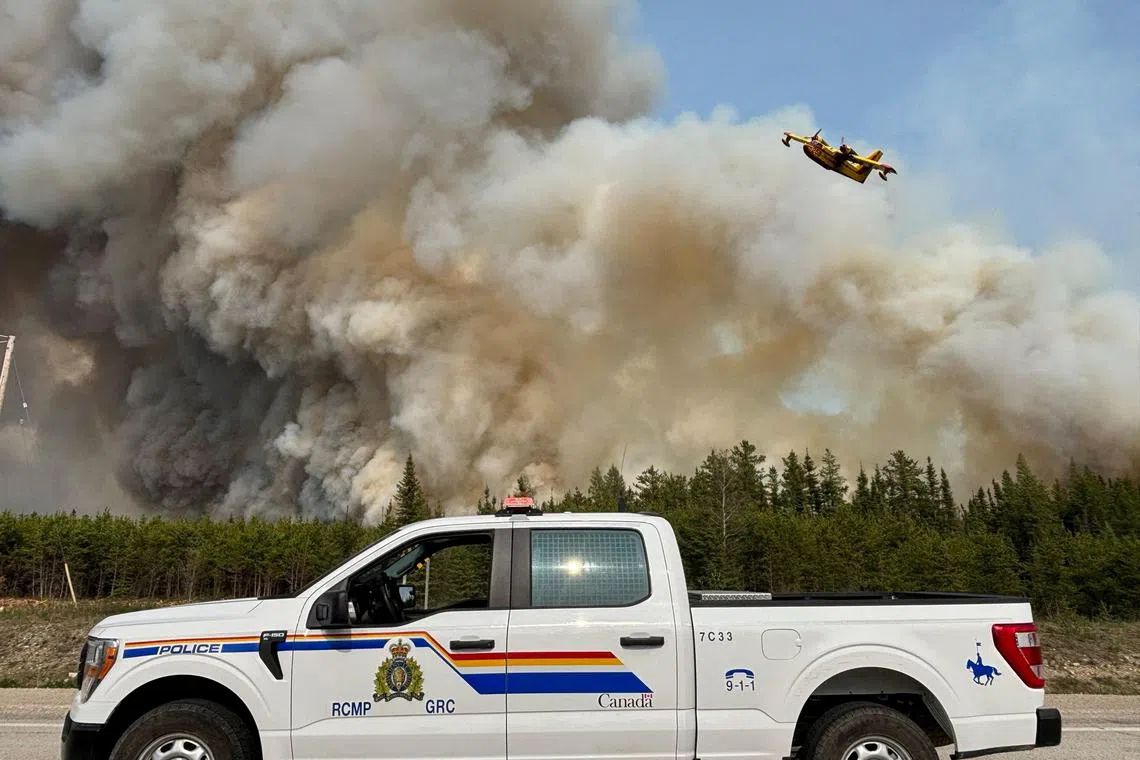 FILE PHOTO: A Royal Canadian Mounted Police (RCMP) patrol vehicle is parked as a water bomber flies over the plume of smoke from a wildfire near The Pas, Manitoba, Canada May 27, 2025. Manitoba RCMP/Handout via REUTERS