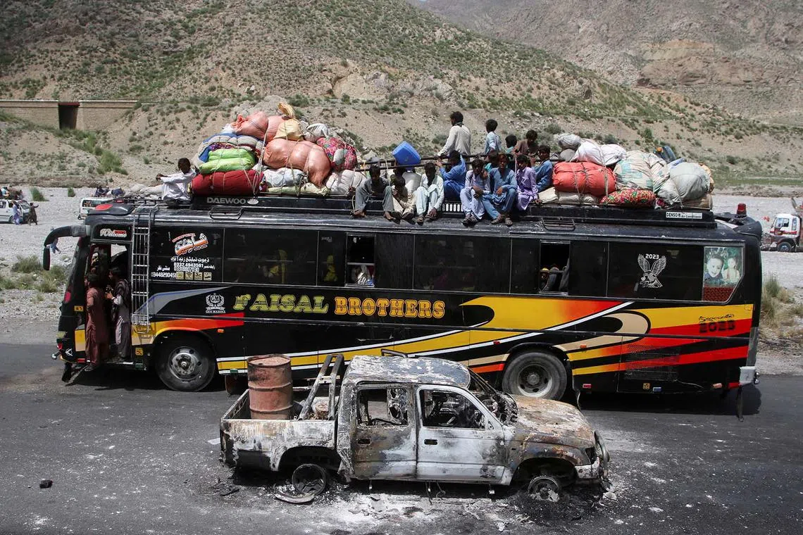 A bus with passengers sitting on the roof with belongings, drives past a damaged vehicle, a day after separatist militants conducted deadly attacks, in Bolan district of Pakistan's restive province of Balochistan, Pakistan, Aug 27, 2024.