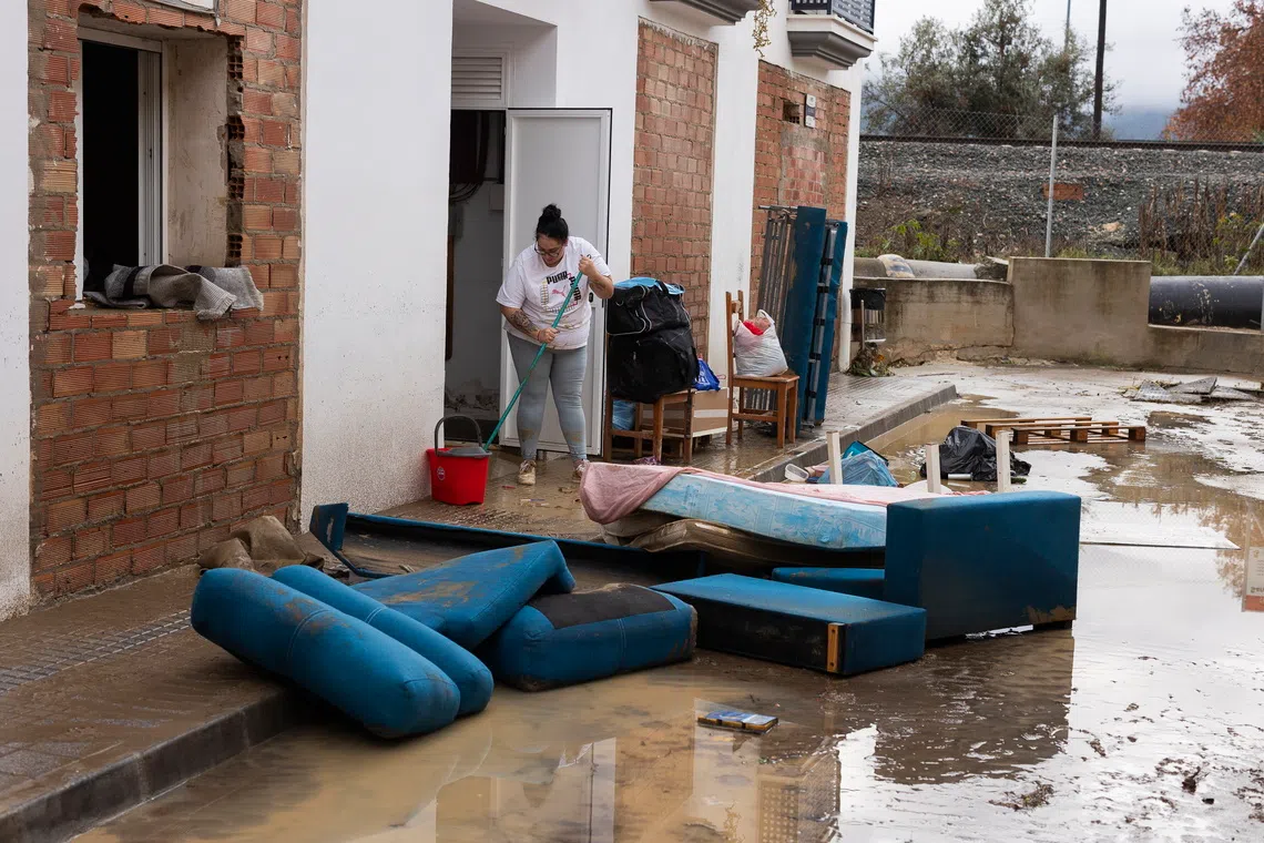 A resident cleans the access to her home the morning after floods affected several parts of the town of Estacion de Cartama.