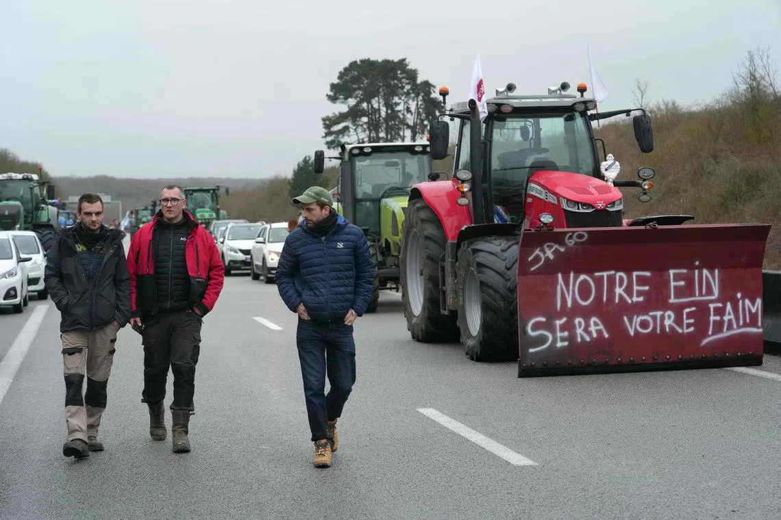 A tractor displaying a placard saying "our end will be your hunger" as farmers block the A16 highway near Amblainville, north of Paris, on Jan 26, 2024.