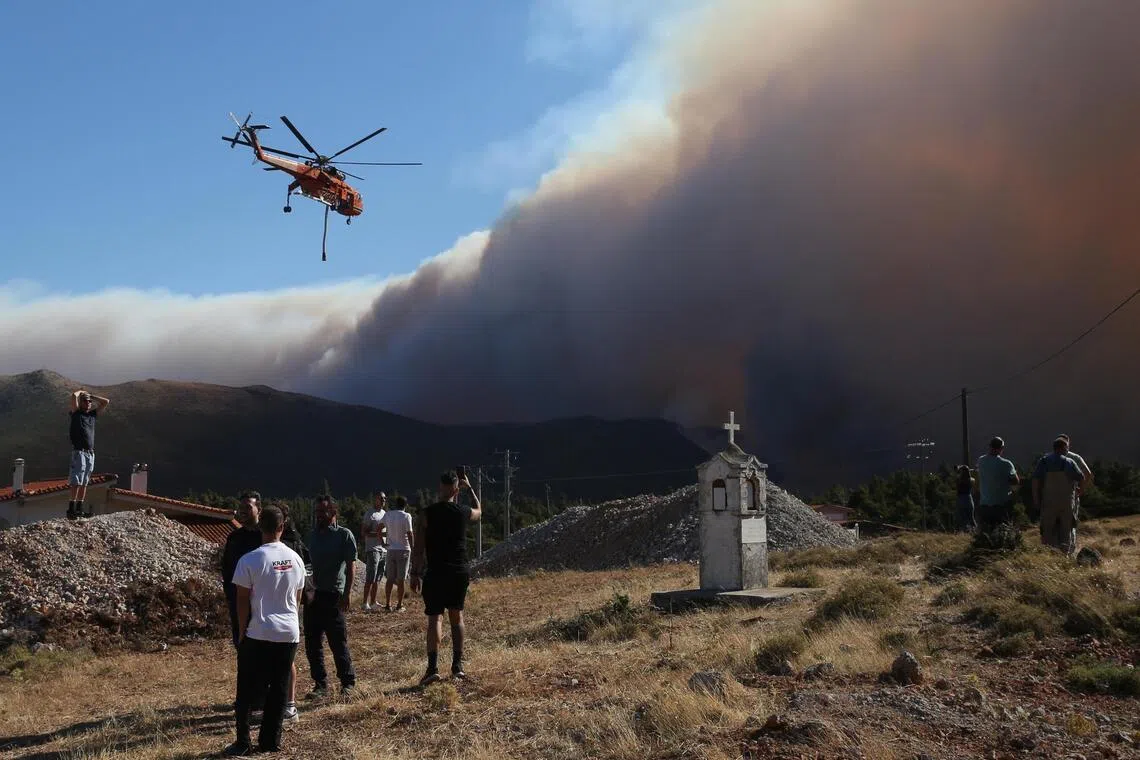 People watch a large smoke plume while a helicopter flies overhead.