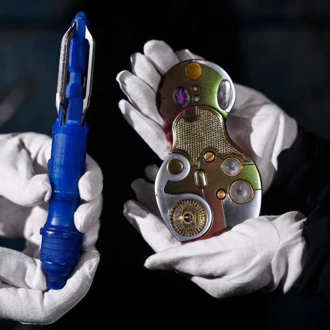 This photo taken on January 30, 2026 shows gallery assistants posing with the 'Fourteenth Doctor’s Rehearsal Sonic Screwdriver' (L) and the 'Fifteenth Doctor’s Joy To The World Hero Light-Up Sonic Screwdriver' (R), props from the popular long-running Britain series "Doctor Who", at a preview by memorabilia auction house Propstore in Rickmansworth, near London. From a Tardis to a Dalek, "Doctor Who" fans worldwide can bid from February 3 to own a piece of television history as the BBC auctions off props and costumes from the cult sci-fi series. The 17-day online auction features items from the modern era of the decades-spanning show, which first appeared on British TV in 1963 and then relaunched in 2005 after a 16-year small-screen hiatus. (Photo by HENRY NICHOLLS / AFP)