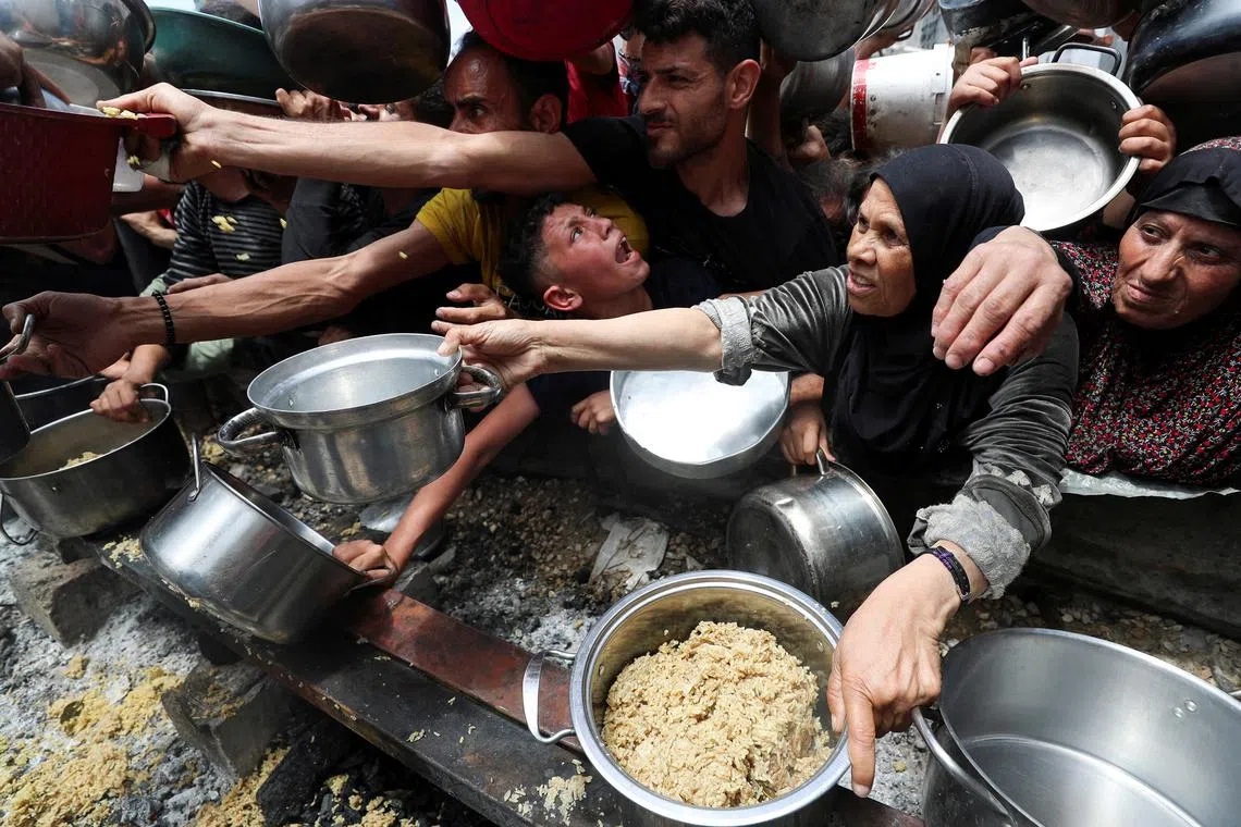 Palestinians wait to receive food cooked by a charity kitchen, in Jabalia, in the northern Gaza Strip, May 14, 2025. REUTERS/Mahmoud Issa