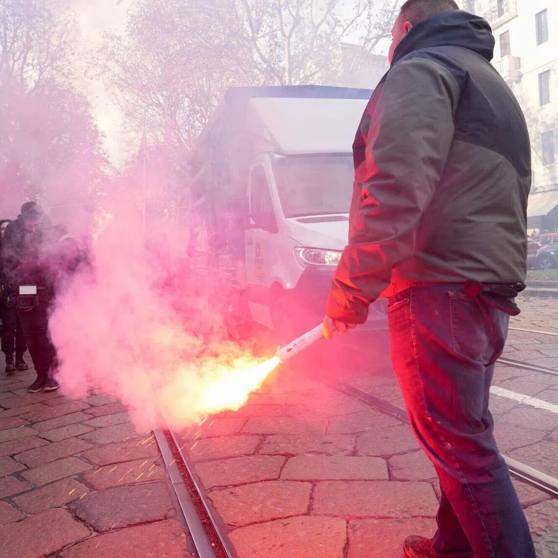 A protester holds a flare during a demonstration in Milan, Italy, amid rising domestic tensions over the Winter Games.