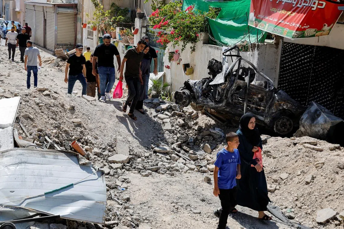 Palestinians walk through a damaged road following an Israeli operation in Jenin.