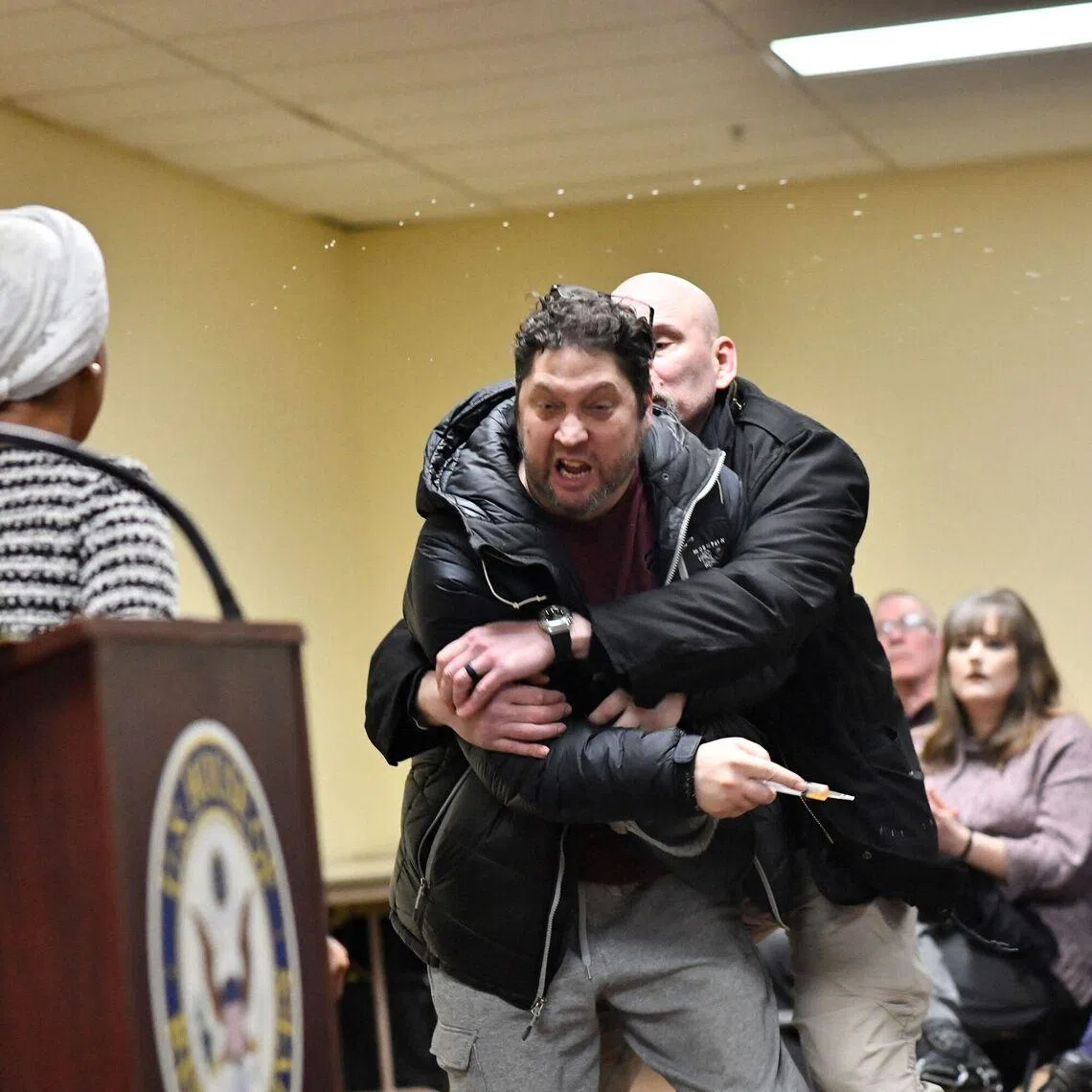A man is tackled after spraying an unknown substance at US Representative Ilhan Omar (left) during a town hall in Minneapolis on Jan 27.