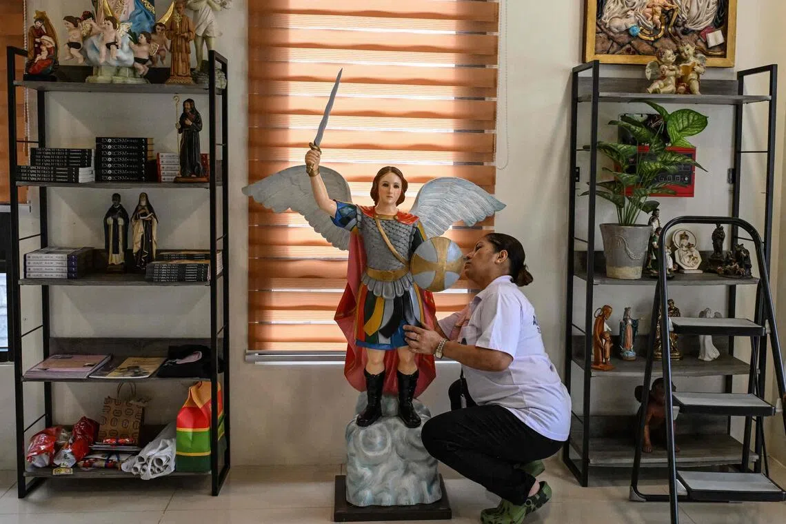 A woman cleaning a statue of a saint displayed alongside books about exorcism at the Saint Michael Center for Spiritual Liberation and Exorcism in Makati, Metro Manila.