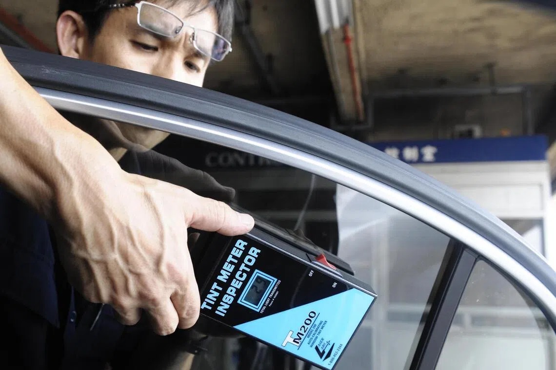 A vehicle inspector using a tint meter to measure the amount of light passing through a car window.