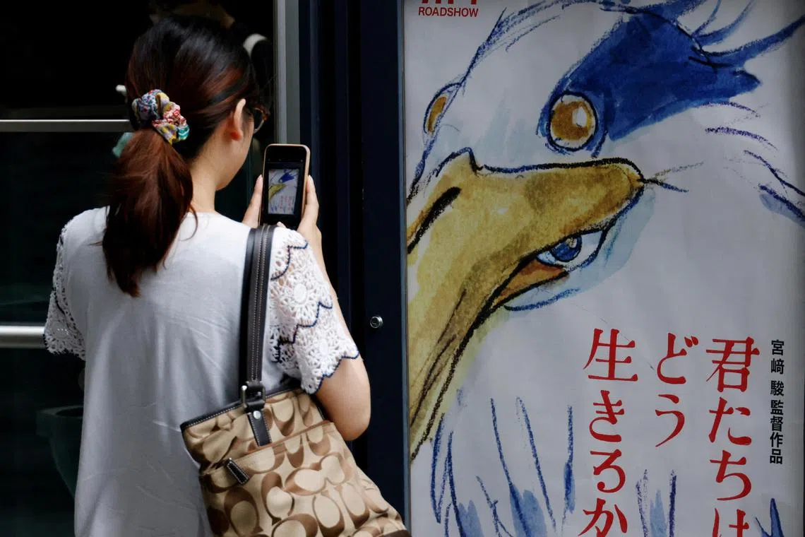 A woman takes a picture of a movie poster for Oscar-winning Japanese animation master Hayao Miyazaki's film How Do You Live? (Kimitachi Wa Do Ikiru Ka?) outside a movie theatre in Tokyo, Japan, on July 14, 2023. 
