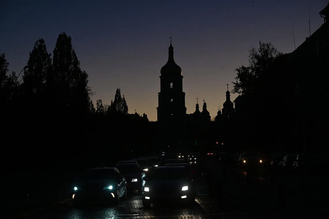 Vehicles drive along a street with the St. Sophia Cathedral silhouetted in the background, as Kyiv is plunged into near darkness.   