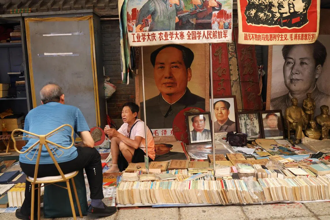A vendor attends to a customer next to images and statues depicting late Chinese chairman Mao Zedong, at the secondhand books section of Panjiayuan antique market in Beijing, China August 3, 2024. REUTERS/Florence Lo