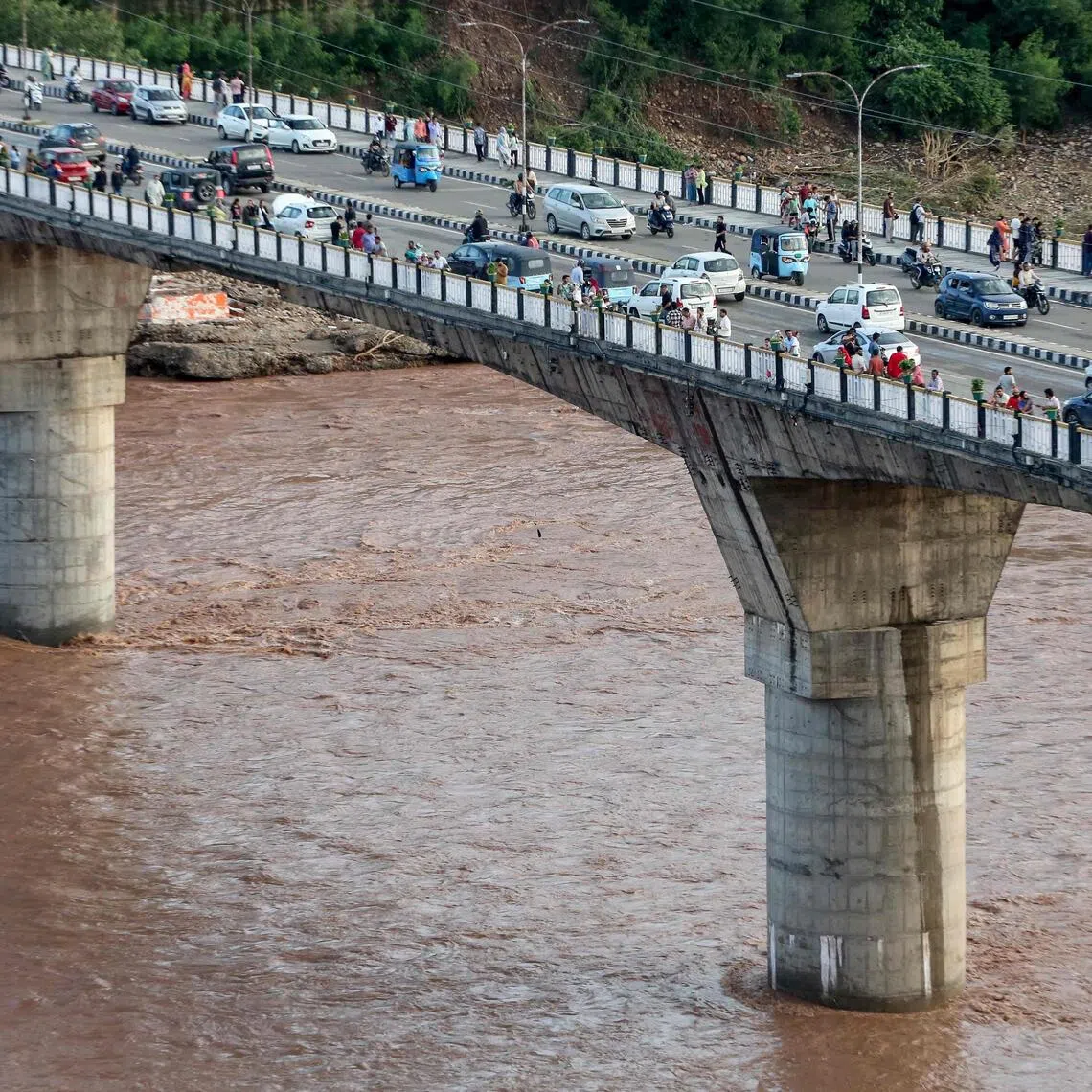 Commuters ride along a bridge across the overflowing Tawi river after heavy rains induced floods in Jammu on Aug 27. 