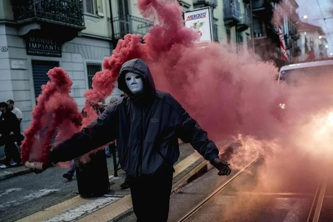 A masked protester holding a smoke flare during a demonstration against rearmament, high fuel prices and data centres in Turin, Italy, on Oct 24.