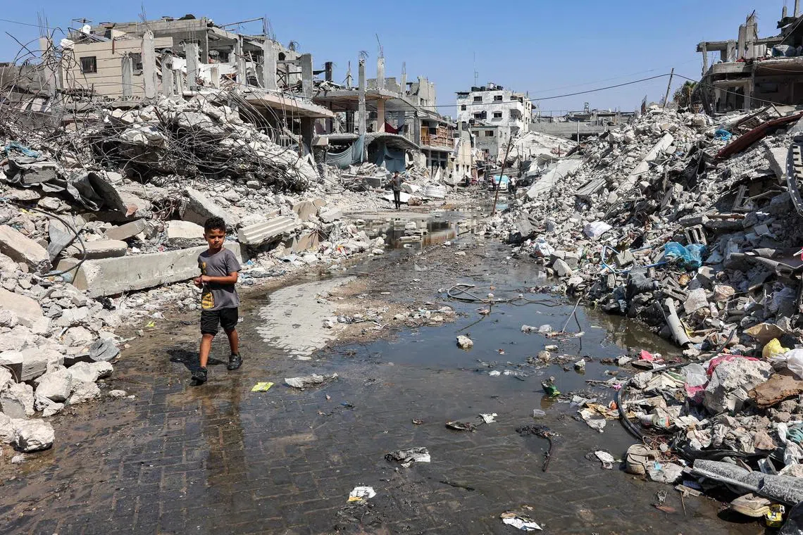 A boy walking through a puddle of waste water, past mounds of trash and rubble, in the northern Gaza Strip, on Aug 14.