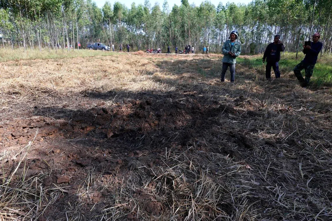 People examine an impact crater in a field following clashes along the Thailand-Cambodia border in Thailand's Sisaket province on Dec 9, 2025.  