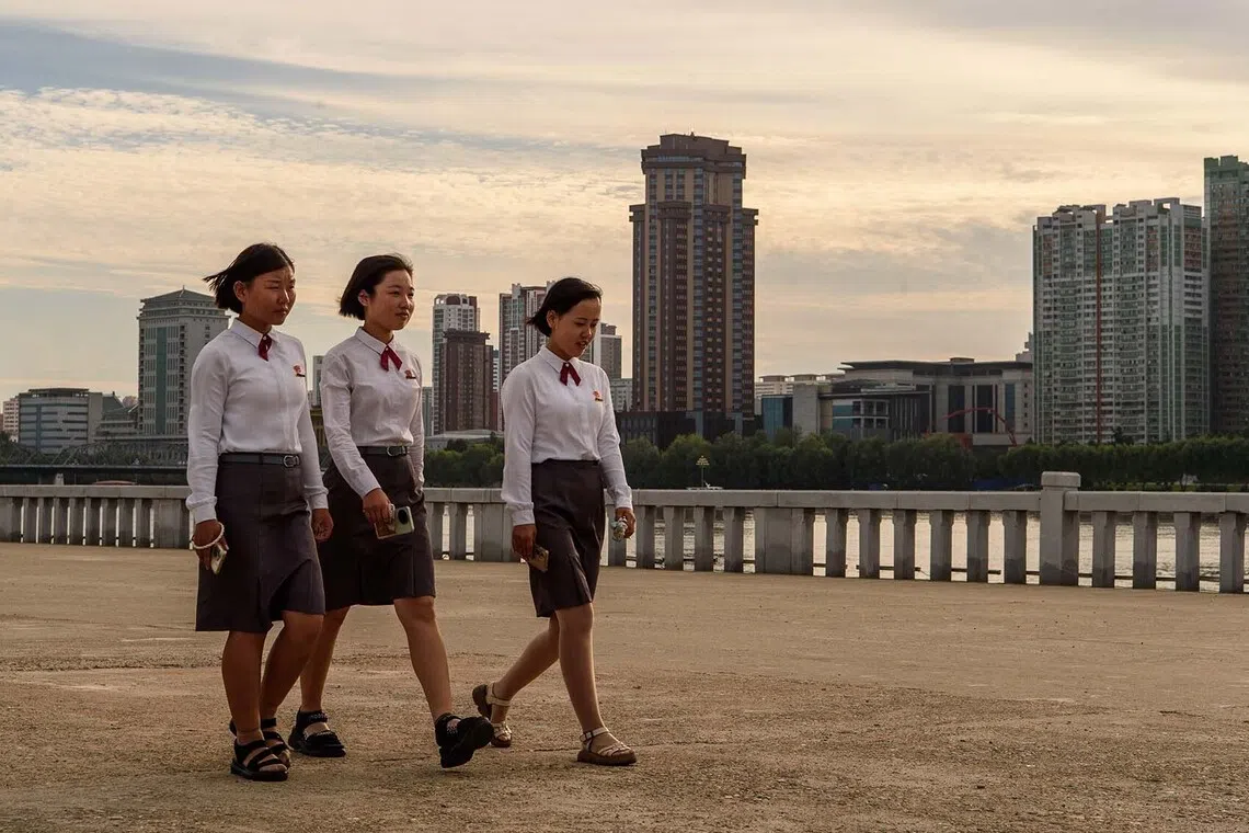 TOPSHOT - Three girls hold mobile phones as they walk along the Taedong River in Pyongyang on August 27, 2026. (Photo by KIM Won Jin / AFP)