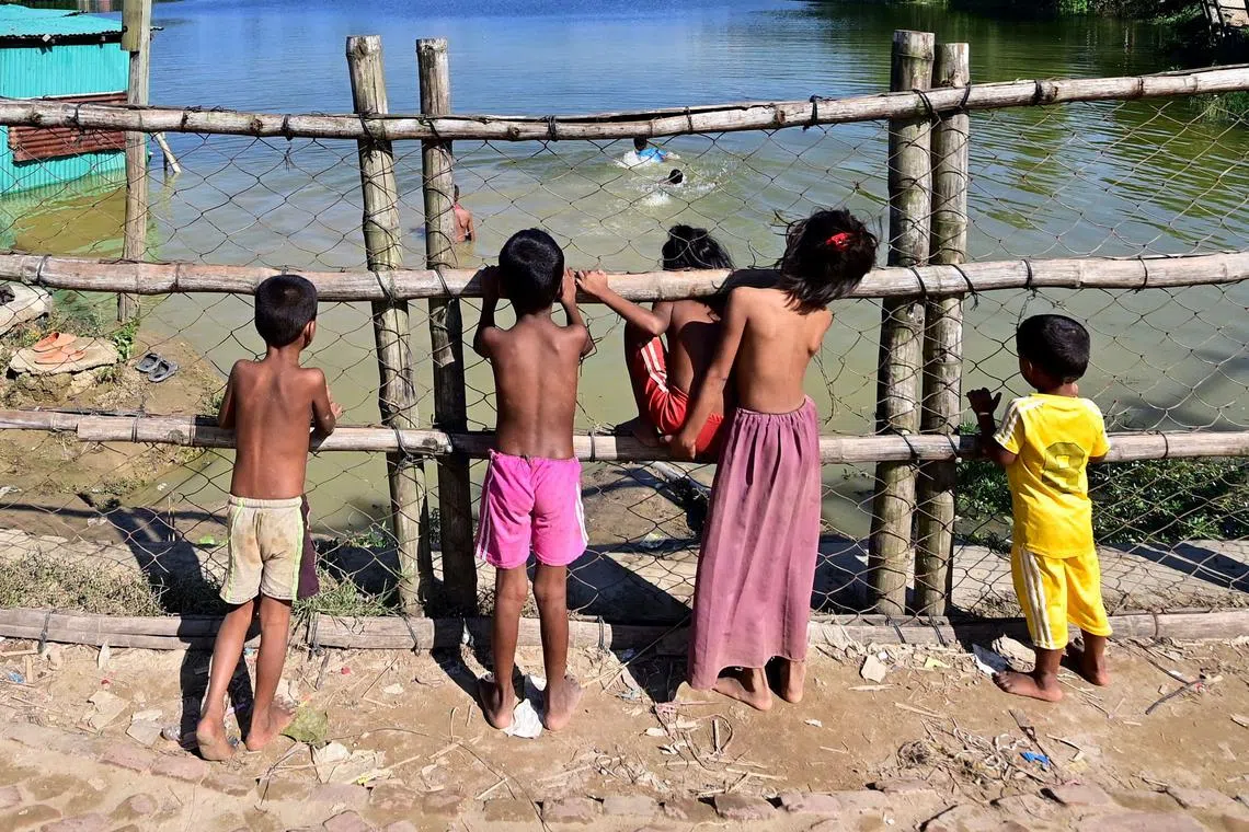 Rohingya refugee children watch boys swimming in a pond at Nayapara refugee camp in Teknaf on Nov 24, 2023.  