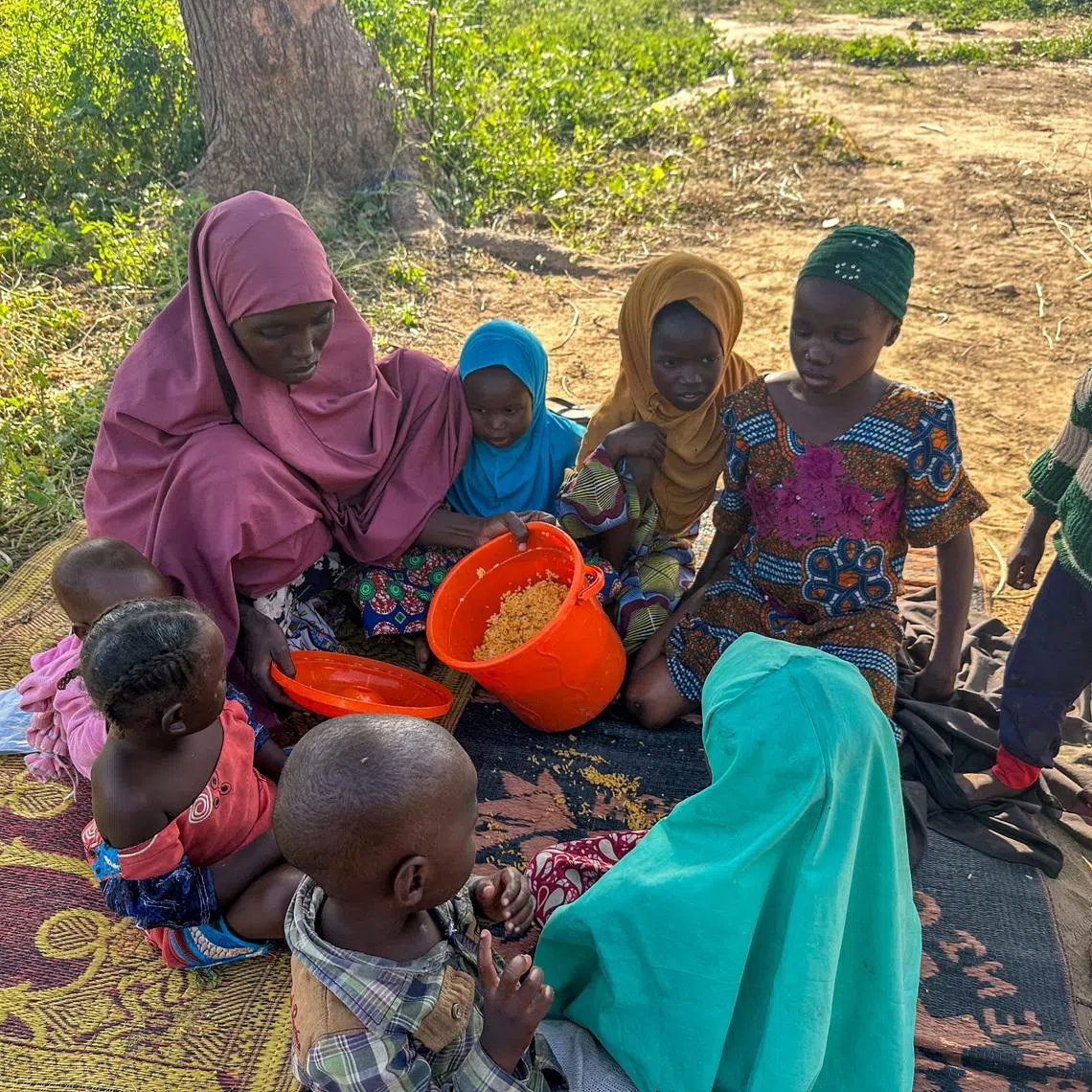 FILE PHOTO: Zainab Abubakar eats cooked food with her children at Gubio IDP camp in Maiduguri, Nigeria October 28, 2024. REUTERS/Abraham Achirga/File Photo