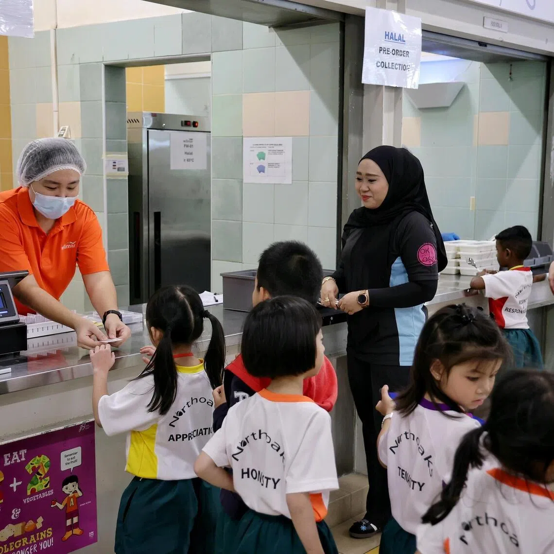 Northoaks Primary School pupils queueing to receive number tags before collecting the bento boxes they pre-ordered under the central kitchen meal model during recess time on Jan 12, 2026.