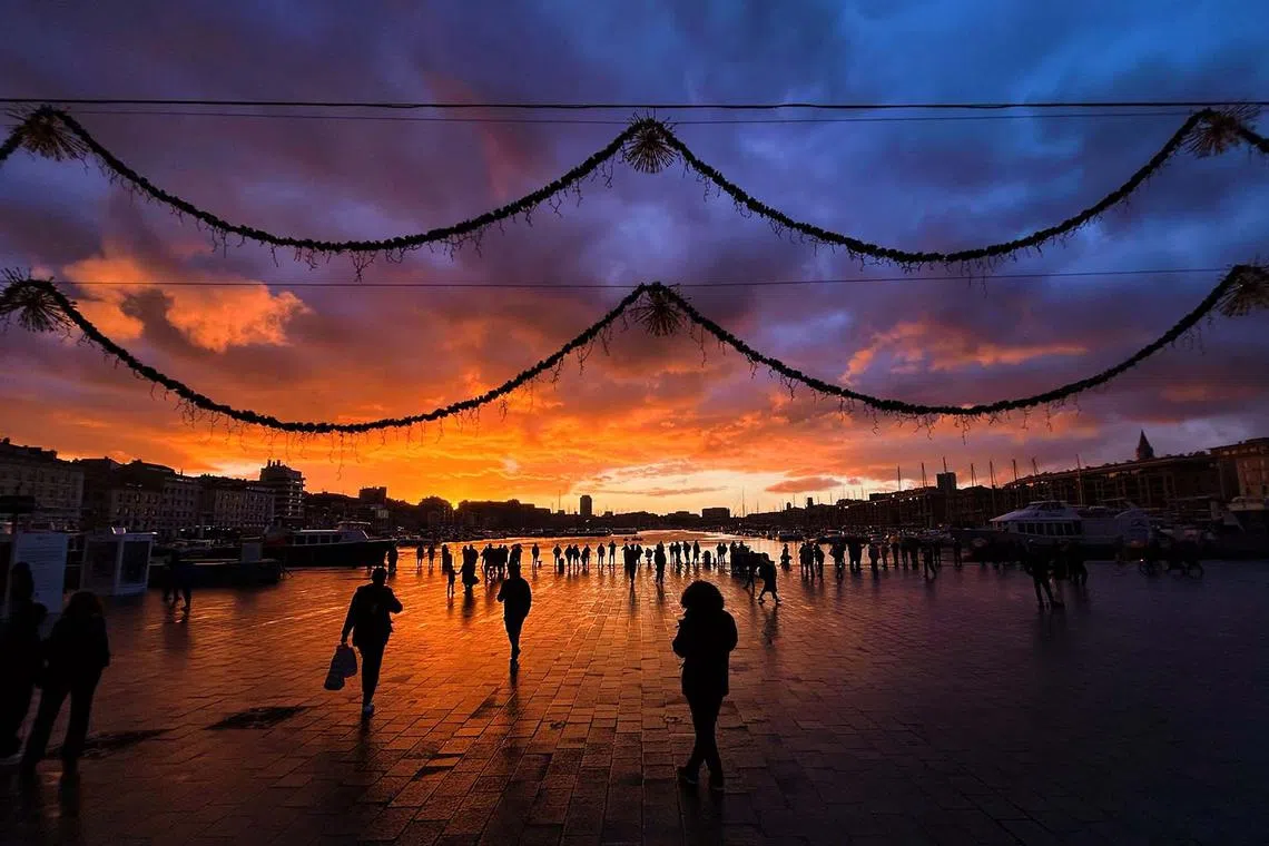 TOPSHOT - People walk along the Vieux-Port (the Old Port) at sunset in Marseille, southern France, on December 4, 2023. (Photo by Nicolas TUCAT / AFP)