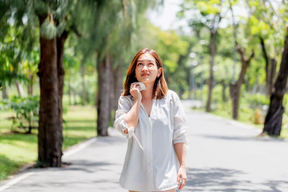 akcool - Istockphoto - Woman walking in the park having sunstroke in summer hot weather, Young pretty girl drying sweat using a wipe on a warm summer day in a park
