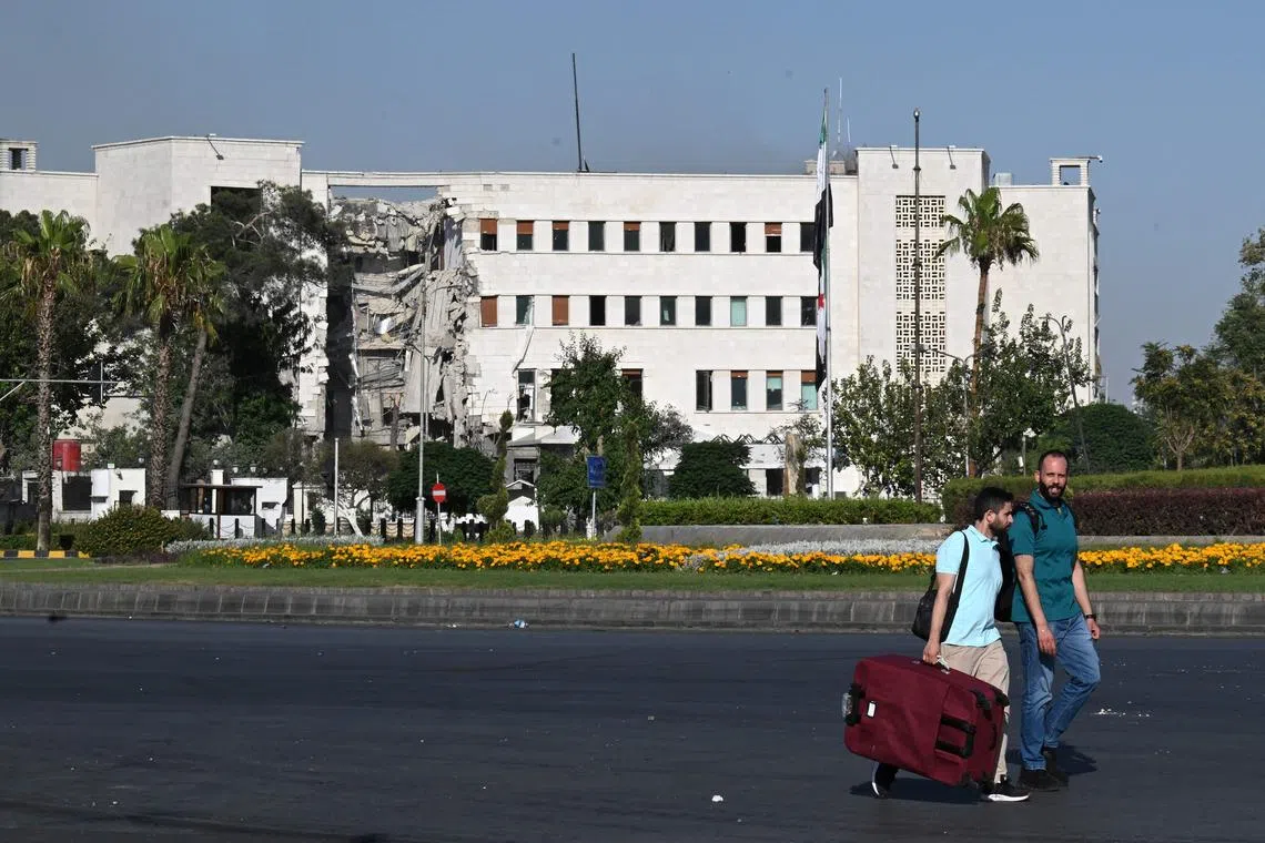 People walk in front of the heavily damaged Syrian army and Defence Ministry headquarters in Damascus, following Israeli strikes on July 16, 2025. 
