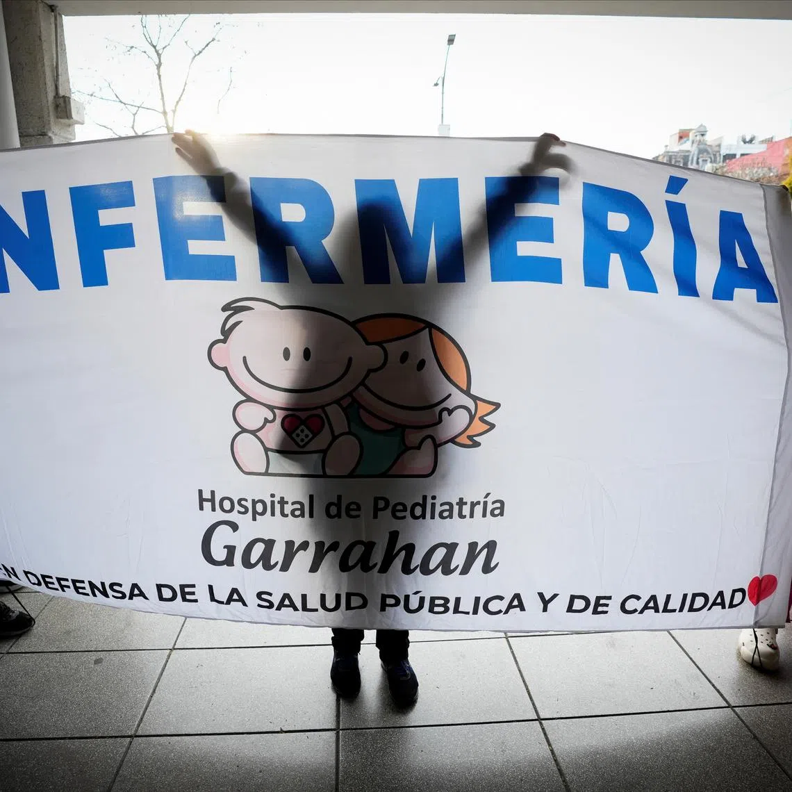 Pamela Barraza, a nurse at Garrahan children's hospital, a leading center for pediatric surgery and organ transplants that is now at the heart of the country's escalating public hospital crisis, holds a banner that reads \"Nursing\", outside the hospital, in Buenos Aires, Argentina, August 13, 2025. REUTERS/Mariana Nedelcu
