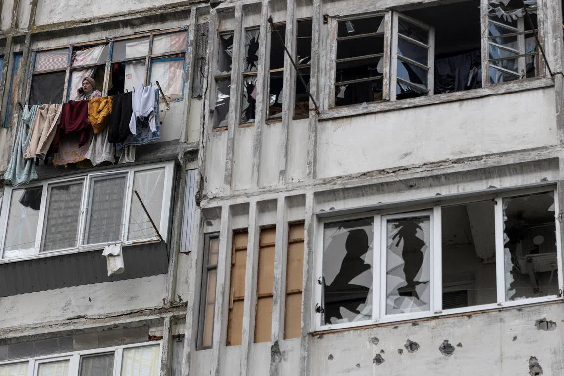 A woman speaks on her mobile phone in the window of a residential building damaged by a Russian strike, in Kherson.