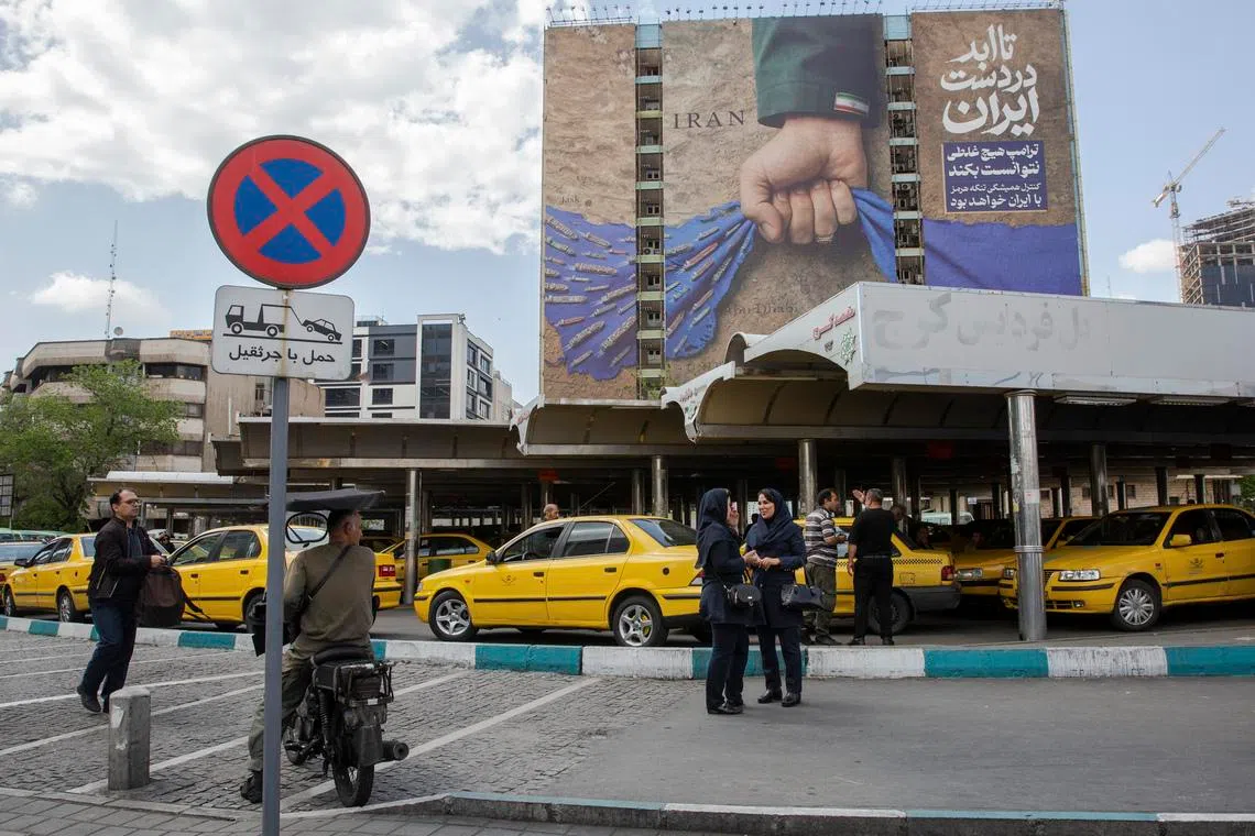 People pass near a billboard depicting a hand representing Iran holding the Strait of Hormuz, in Tehran, Iran, on April 21.