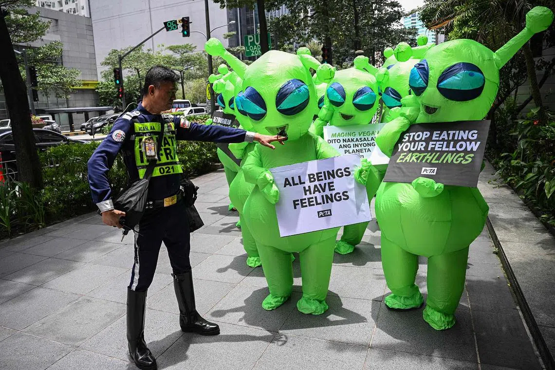 A security guard gestures to members of People for the Ethical Treatment of Animals (PETA) wearing alien outfits during a protest in the financial district of Manila on July 31, 2025, as part of their campaign for people to eat vegan, and highlighting greenhouse gas emissions from agriculture. (Photo by TED ALJIBE / AFP)