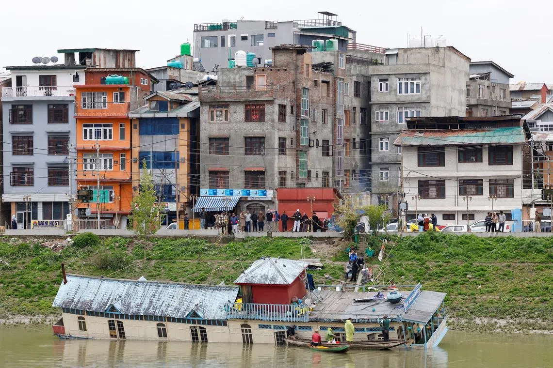 Locals watching as people retrieve belongings from a partially sunken houseboat after it developed a hole, along the banks of the Jhelum River in Srinagar, Indian Kashmir, April 8, 2026. 
