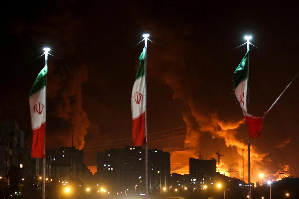 Iranian flags fly as fire and smoke from an Israeli attack on Sharan Oil depot rise, following Israeli strikes on Iran, in Tehran, Iran, June 15, 2025. Majid Asgaripour/WANA (West Asia News Agency) via REUTERS