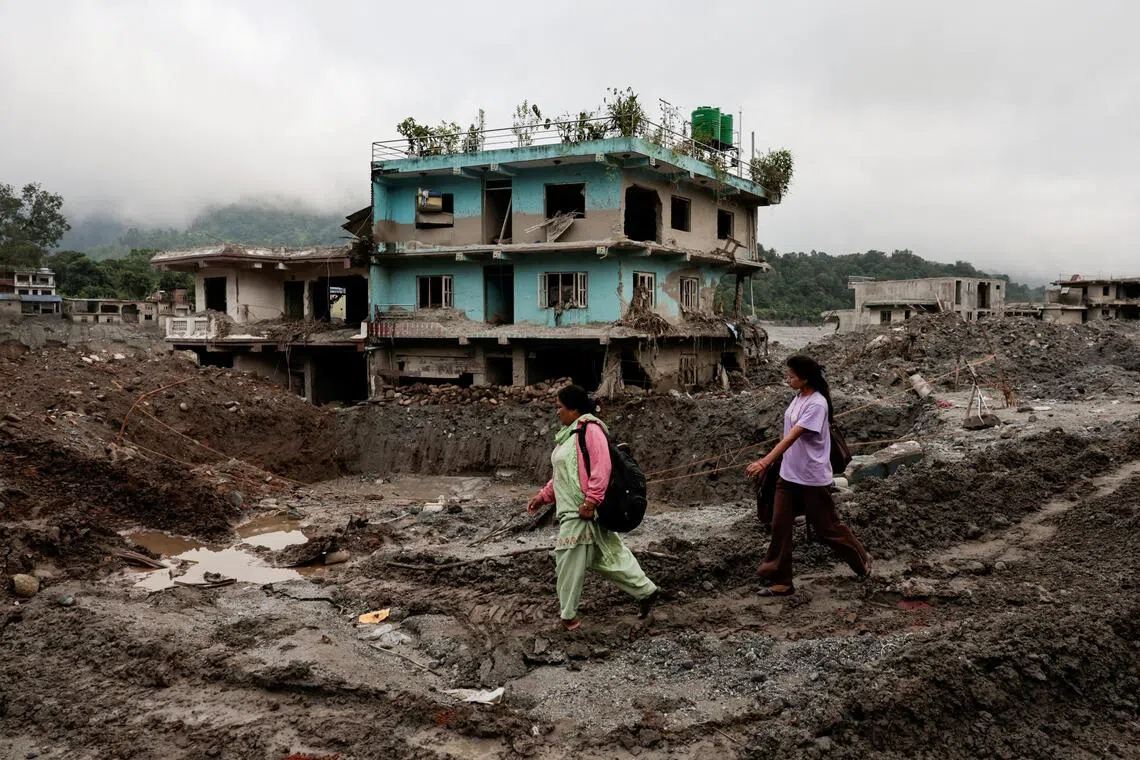 People walking past damaged houses in Devighat, Nuwakot district in Nepal on Sept 21, following deadly flash floods and a mudslide in August.