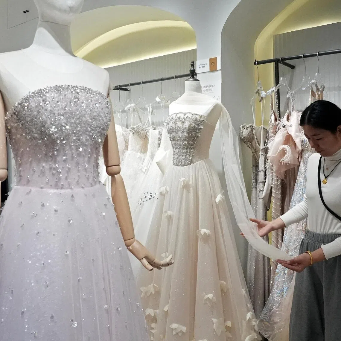 Wedding dress seller Zhu Jiaomei inspects a gown's fabric at Huqiu Bridal City in Suzhou, Jiangsu province, China January 16, 2026. REUTERS/Nicoco Chan