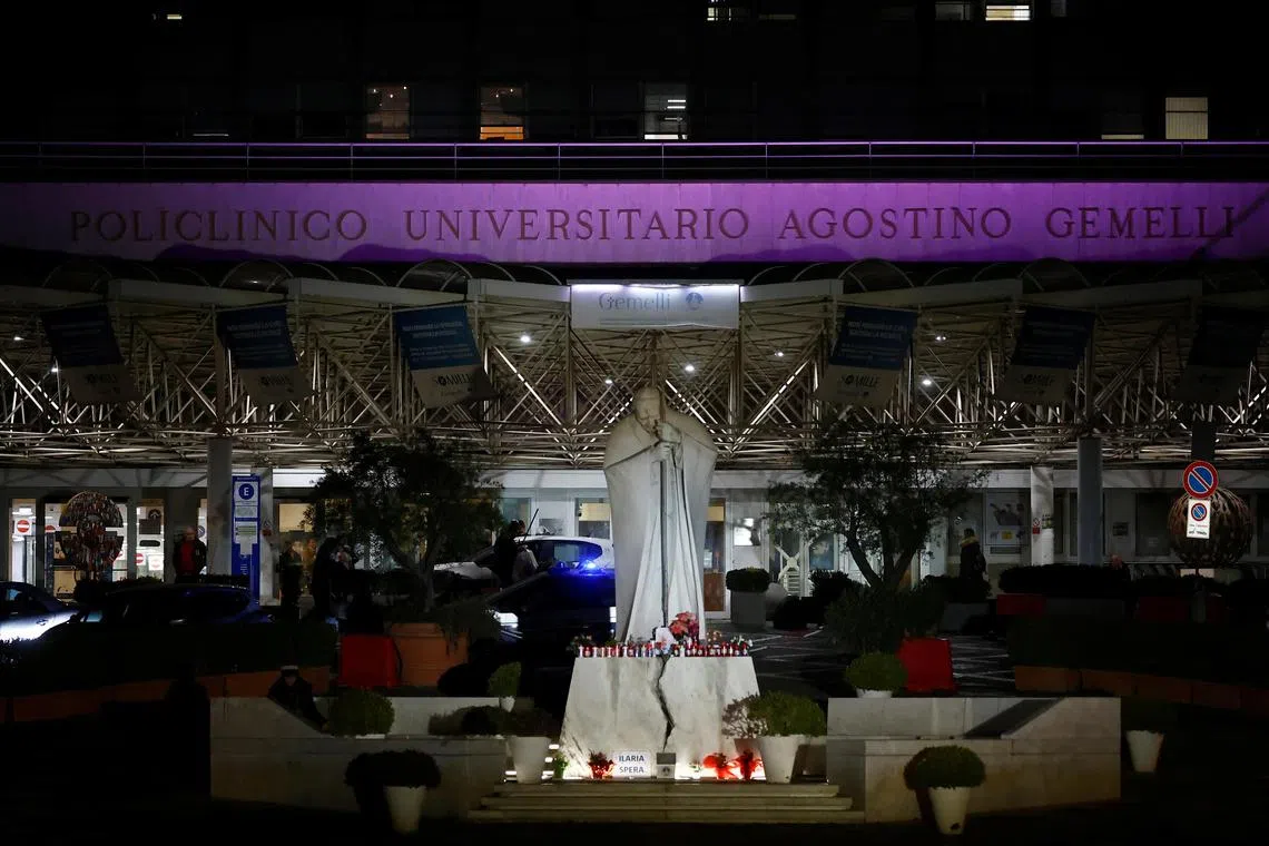 Decorated candles, flowers, and pictures of Pope Francis are placed at the base of the statue of the late Pope John Paul II in front of Rome's Gemelli Hospital, where Pope Francis is undergoing treatment, on Feb 22. 
