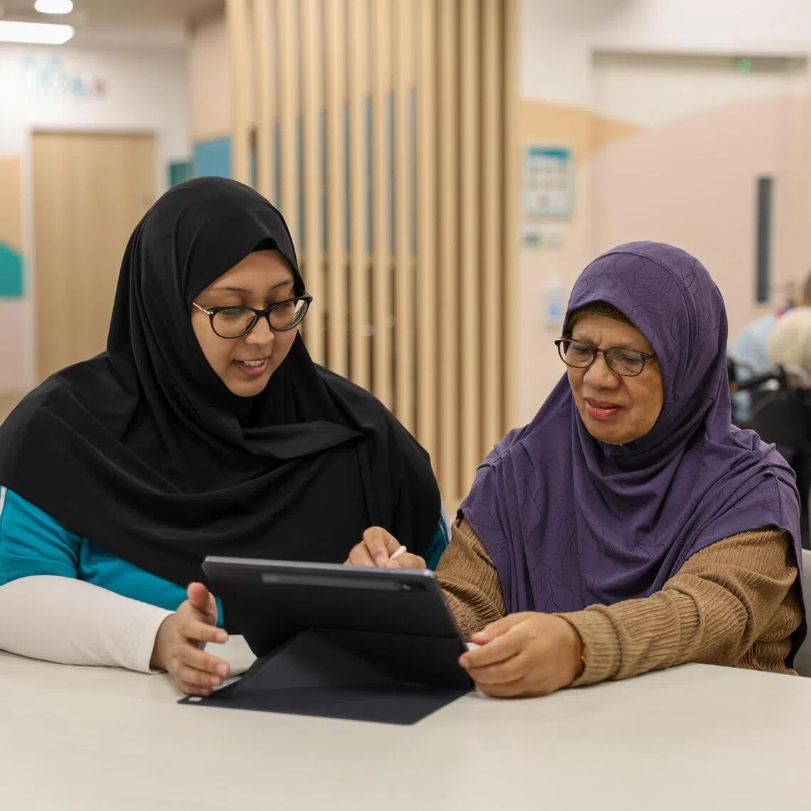 Madam Maria Hadi, who was diagnosed with dementia in 2025, playing a cognitive game at NTUC Health’s Day Centre for Seniors in Kampung Admiralty. With her is NTUC Health staff member Kamaria Md Yassin.