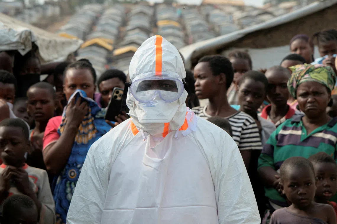 FILE PHOTO: A health worker in personal protective equipment (PPE) stands near displaced people waiting for the burial of suspected Ebola victims at the Kigonze displaced persons camp, one month after an outbreak was declared, in Bunia, eastern Democratic Republic of Congo, June 18, 2026. REUTERS/Gradel Muyisa Mumbere/File Photo