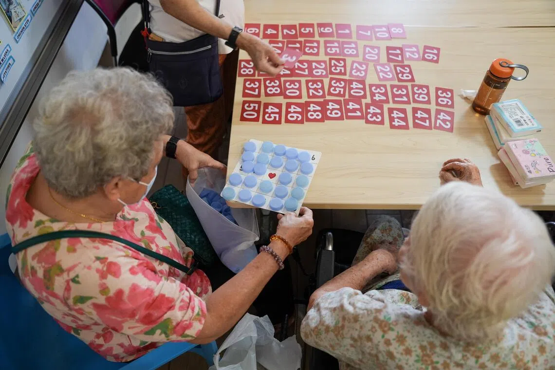 Cheong Yoke Keng, 75, (left) helping a resident at Ren Ci @ Ang Mo Kio with her bingo card on Jun 26.