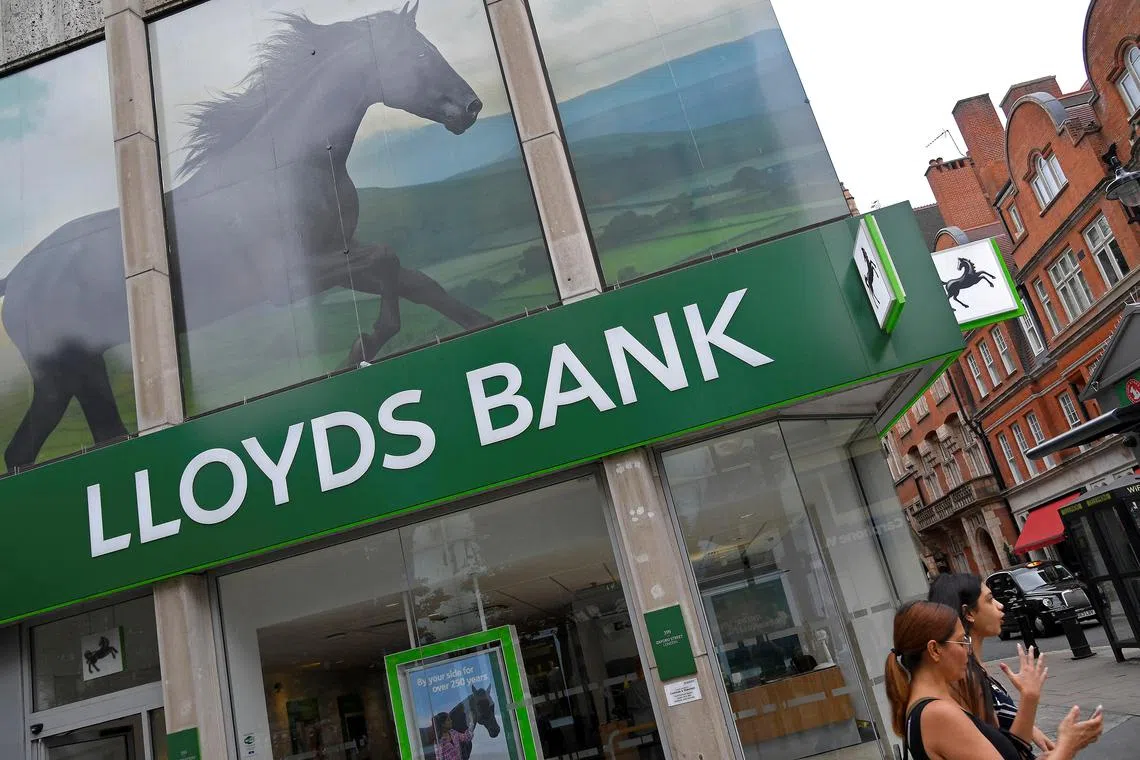FILE PHOTO: A woman looks at her phone as she walks past a branch of Lloyds bank in London, Britain, July 20, 2018. REUTERS/Toby Melville/File Photo
